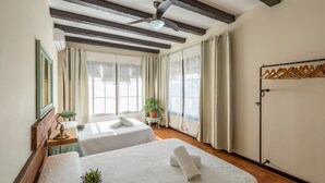 A hotel room with two beds, a ceiling fan, a window with curtains, a small table with a lamp, and a coat rack. - Holiday Home "Casa Rural La Teja" with Pool, Garden and Wi-Fi (Marchena)
