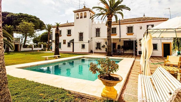 Un grande edificio con piscina, area salotto esterna e zona coperta.