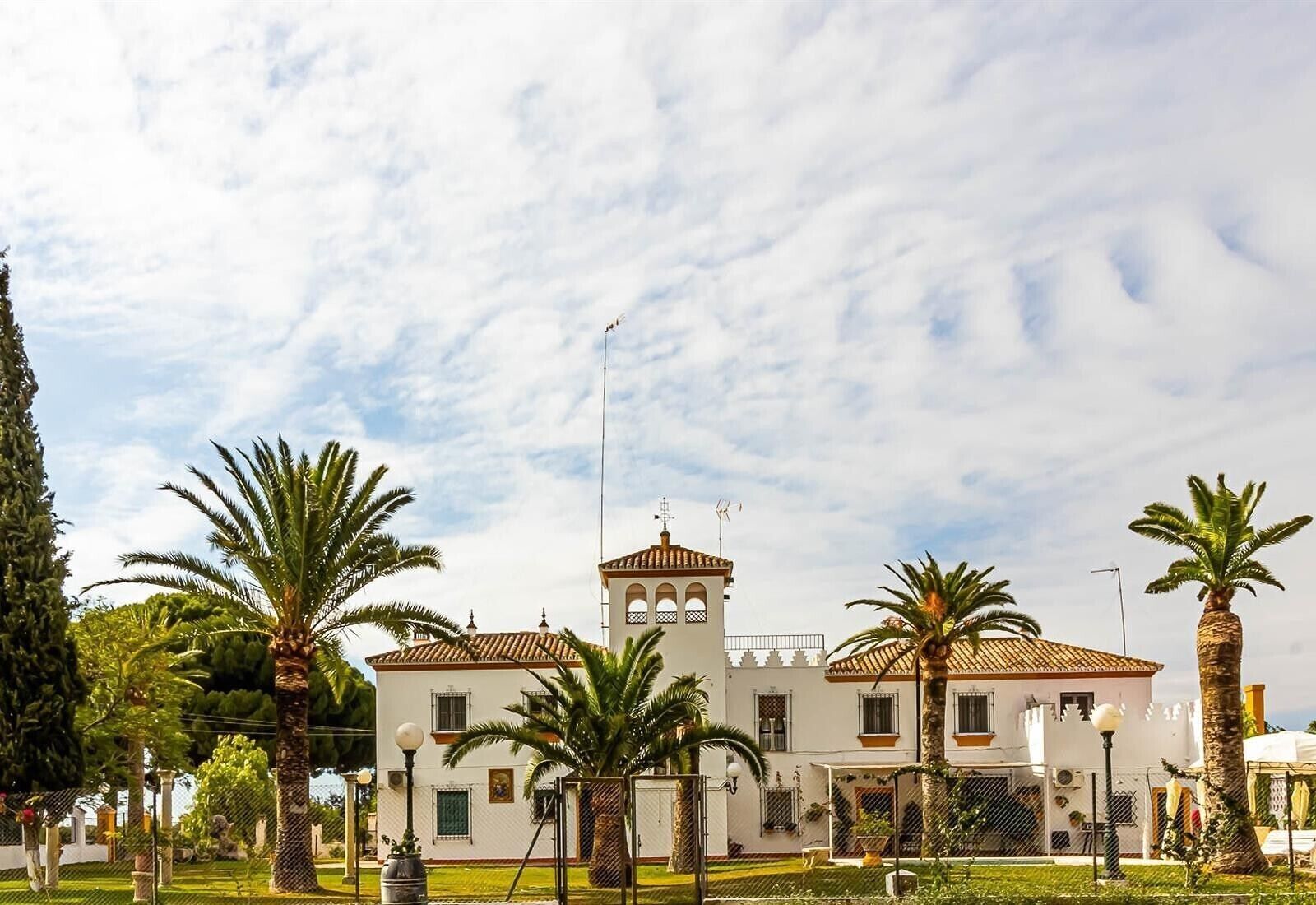 Un edificio con una torre, rodeado de palmeras y un cielo despejado.