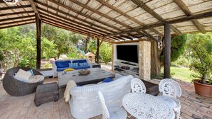An outdoor patio with wicker furniture, a flat-screen TV, and a stone wall. - Quinta das Achadas - Jasmine in Lagos with Shared Pool, Nature & Breakfast (Lagos)