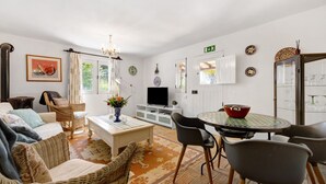 A living room with a sofa, chairs, a coffee table, a TV, and a dining area with a table and chairs. - Quinta das Achadas - Jasmine in Lagos with Shared Pool, Nature & Breakfast (Lagos)