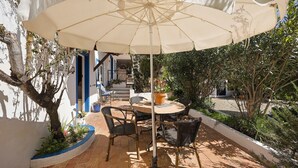 Une terrasse extérieure avec une table ronde et des chaises, un grand parasol et une plante en pot.