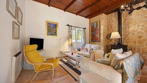 Un salon avec un mur en pierre, un fauteuil jaune, un canapé blanc, une télévision et une cheminée.