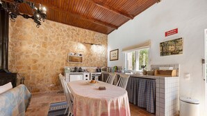 Une cuisine aux murs de pierre, avec une table à manger, des chaises et un luminaire suspendu.