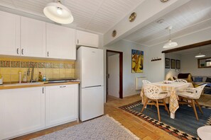 A kitchen with white cabinets, a refrigerator, and a dining area with a table and chairs. - Quinta das Achadas – Mimosa in Lagos with Shared Pool, Nature & Breakfast Included (Lagos)