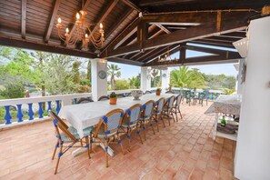 Une terrasse extérieure avec une table et des chaises, une pergola dotée d’un plafond en bois et une vue sur la verdure.