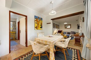 A dining area with a table set for four, surrounded by chairs, a ceiling fan, and a painting on the wall. - Quinta das Achadas – Mimosa in Lagos with Shared Pool, Nature & Breakfast Included (Lagos)