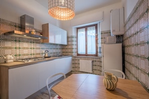 Eine Küche mit einer Holz Arbeitsplatte, weißen Schränken, einer Edelstahl-Dunstabzugshaube, einer Hängeleuchte, einem Fenster mit Vorhängen und Wandtapete mit Muster.