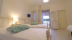 Ein Schlafzimmer mit zwei Betten, einem Nachttisch mit Lampe, einem an der Wand befestigten Fernseher und einer Tür zu einem Außenbereich.