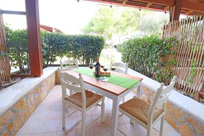 Une terrasse avec une table et des chaises, une bouteille de vin et une nappe verte.