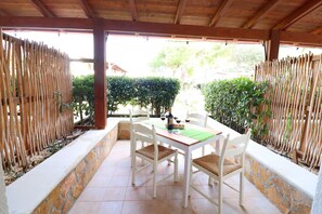 Une terrasse couverte, dotée d’une table et de chaises, entourée de clôtures en bambou et de murs en pierre.