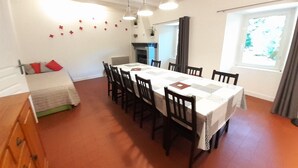 A dining area with a long table, chairs, pendant lights, and a window with curtains. - Gîte "Manoir" with garden by the river, near Clisson (Gétigné)