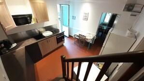 A compact kitchen with modern appliances, a dining area with a table and chairs, and a visible staircase leading to another level. - Gîte "Manoir" with garden by the river, near Clisson (Gétigné)