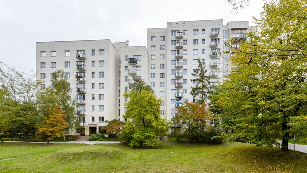 Un edificio residencial de varios pisos con balcones, rodeado por un área verde con árboles.
