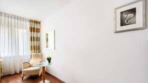 Habitación de hotel moderna con piso de madera, una mesa redonda de vidrio, un sillón beige y un amplio ventanal con cortinas traslúcidas.