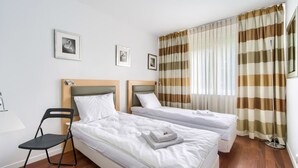 Habitación de hotel con dos camas individuales, una silla y un ventanal con cortinas a rayas.