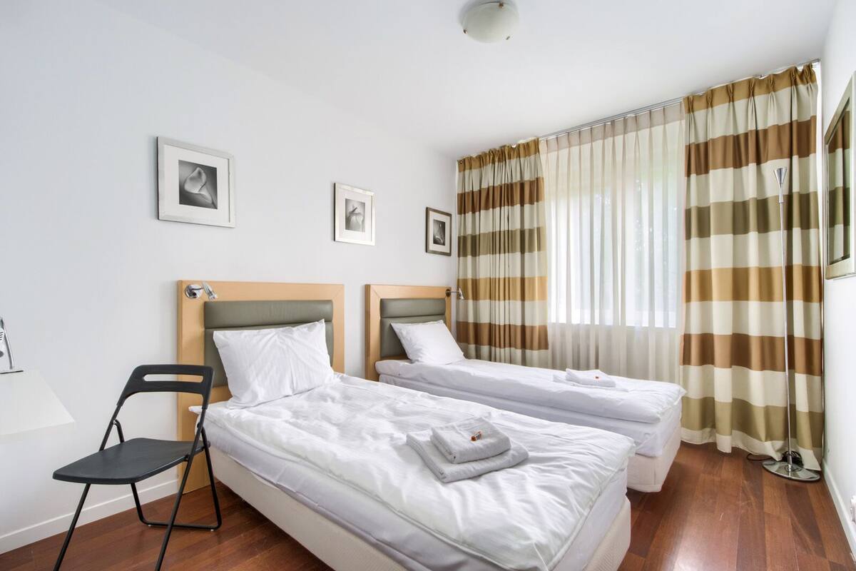 Habitación de hotel con dos camas individuales, una silla y un ventanal con cortinas a rayas.