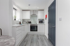 A compact kitchen with white cabinets, a built-in oven, a microwave, and a window above the sink. - The Gateway Apartment 4 (Blackpool)