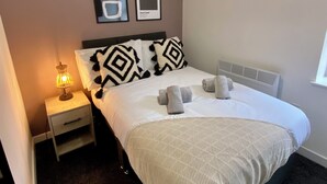 A neatly arranged bedroom with a bed, bedside lamps, a hanging light fixture, and wall art. - The Gateway Apartment 4 (Blackpool)