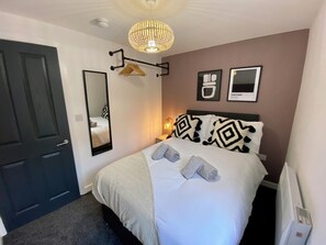 A neatly arranged bedroom with a bed, a hanging light fixture, a mirror, and a wall-mounted heater. - The Gateway Apartment 4 (Blackpool)
