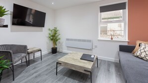 A modern living room with a flat-screen TV, a coffee table, a sofa, and a window with a view. - The Gateway Apartment 4 (Blackpool)