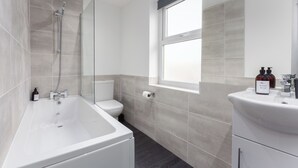 A modern bathroom with a bathtub, toilet, and sink. - The Gateway Apartment 4 (Blackpool)