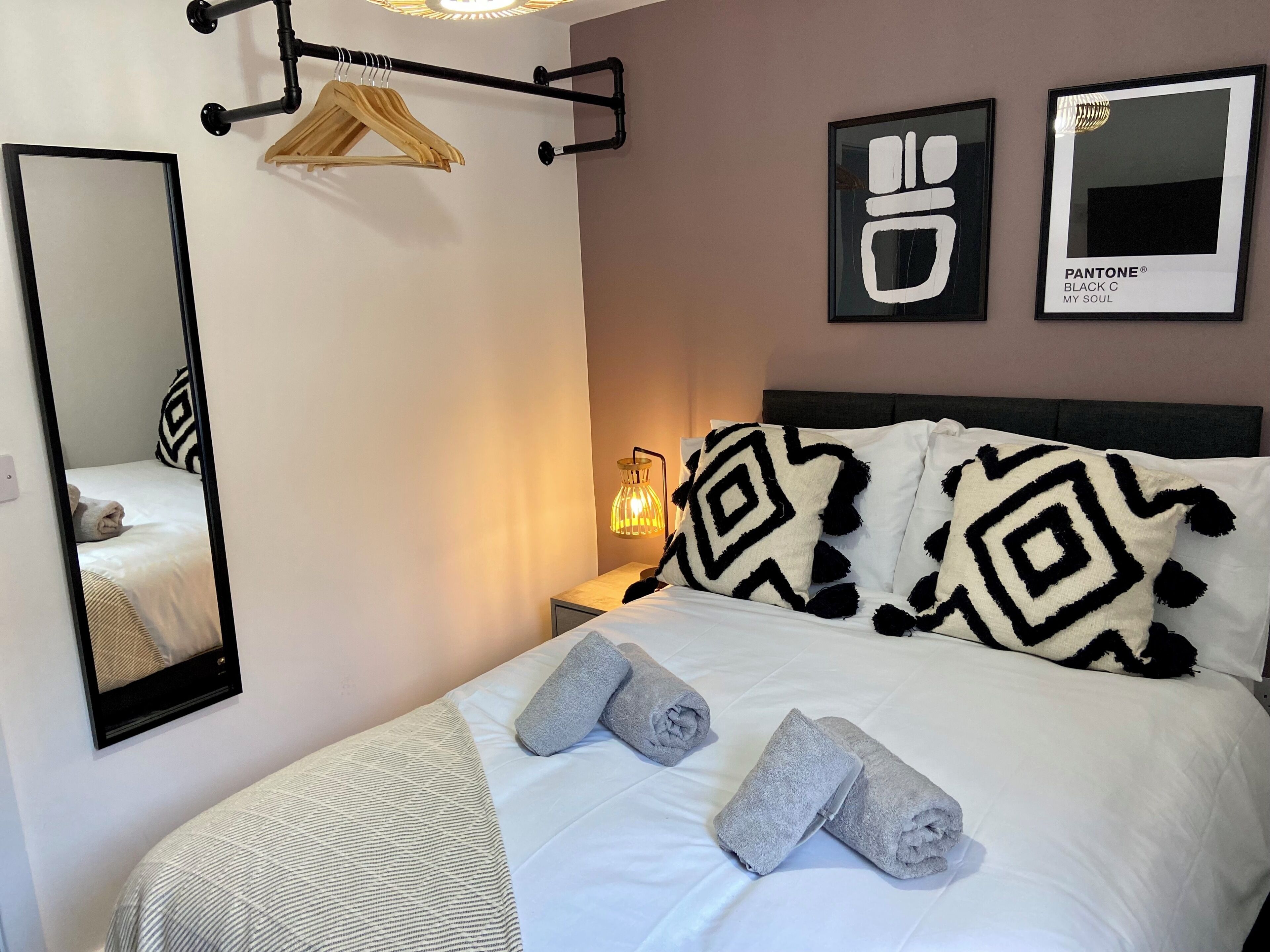 Une chambre d’hôtel comprenant un lit, un porte-vêtements, une table de chevet avec une lampe et un miroir.