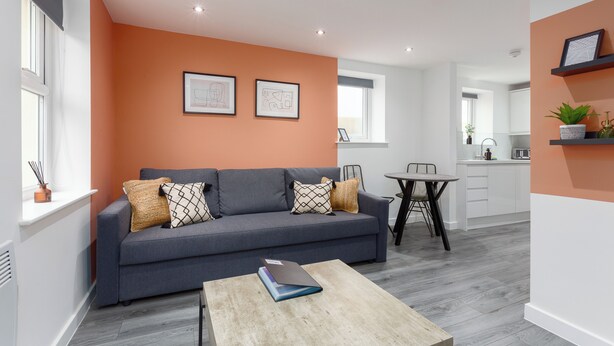 A modern living room with a grey sofa, a wooden coffee table, and a kitchen in the background. - The Gateway Apartment 4 (Blackpool)
