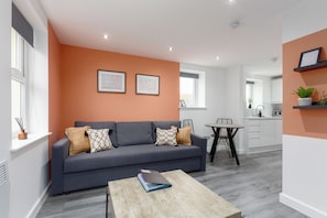 A modern living room with a grey sofa, a wooden coffee table, and a kitchen in the background. - The Gateway Apartment 4 (Blackpool)