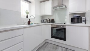 A modern kitchen with white cabinetry, a built-in oven, a microwave, and a window with a plant. - The Gateway Apartment 4 (Blackpool)