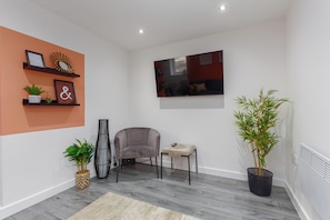 A modern living room with a grey sofa, a small table, a potted plant, and a wall-mounted TV. - The Gateway Apartment 4 (Blackpool)