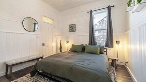 A bedroom with a bed, bench, bedside table, wall-mounted mirror, and window with curtains.