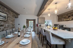 A kitchen with a long wooden table set for dining, a stone wall, and a sign reading "PROSECCO TIME".