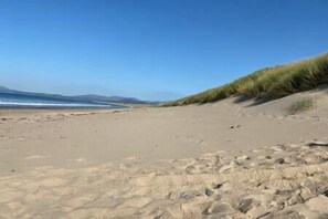 A sandy beach with gentle waves and grassy dunes in the background.
