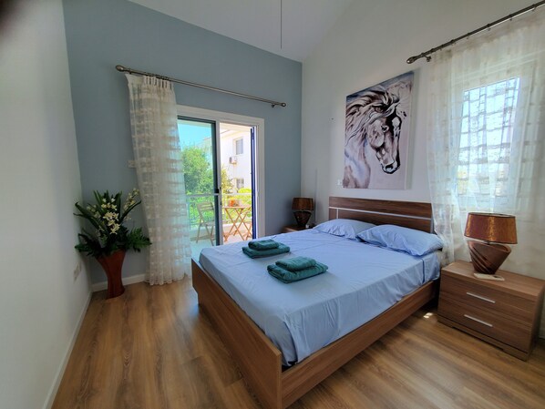 A bedroom with a bed, a nightstand, a potted plant, a window with curtains, and a painting on the wall. - Villa - Sleeps 6, Free Parking & Heated Pool (Paralimni)