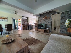 A spacious living area with a stone fireplace, a flat-screen TV, and a dining area with chairs and a table. - Charming 3-bed Villa in Protaras With Heated Pool (Paralimni)