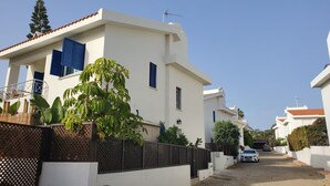 A residential street with modern white houses, a paved road, and a white car parked on the side. - Villa - Sleeps 6, Free Parking & Heated Pool (Paralimni)