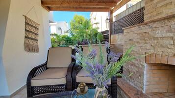 Un área de estar al aire libre con mobiliario de mimbre, una mesa de vidrio y un jarrón decorativo con flores.