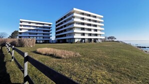 A modern multi-story building with a flat roof and white exterior, located near a body of water. - Welcome to apartment 58 in the house "Berlin". (Großenbrode)