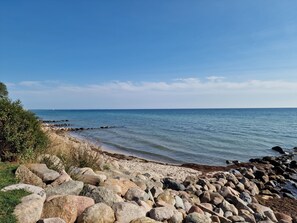 A rocky beach with clear blue water and a distant sailboat.