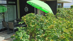 A modern outdoor seating area with a table and chairs, a green umbrella, and lush greenery. - Welcome to apartment 58 in the house "Berlin". (Großenbrode)