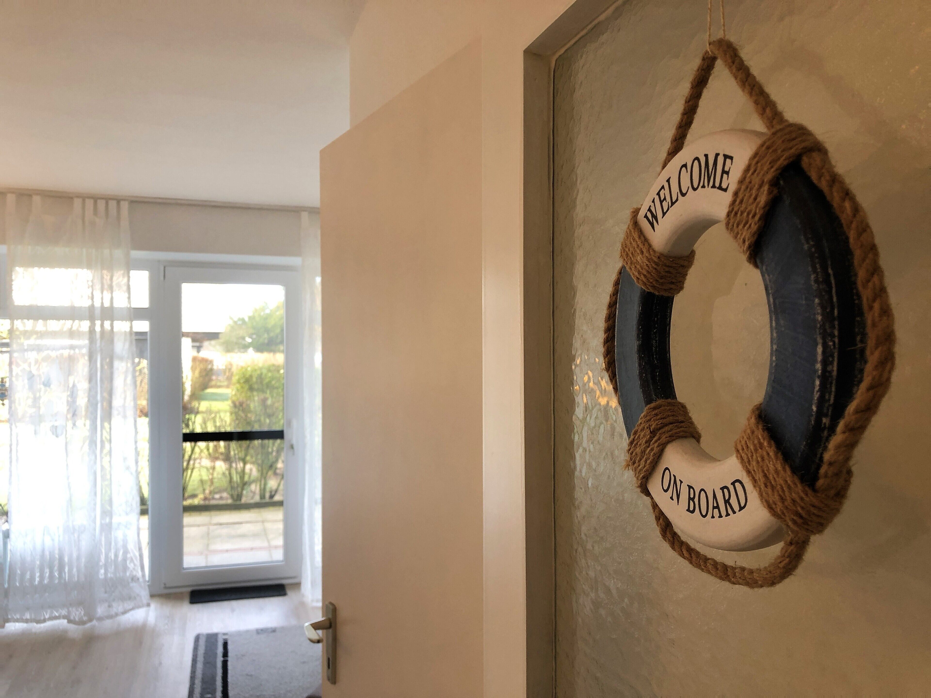 A room with a door leading to a balcony, a welcome sign on the wall, and a view of greenery outside.