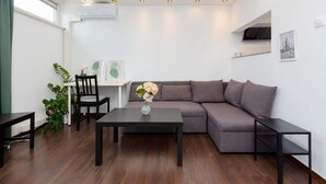 Un salón moderno con un sofá marrón oscuro, una mesa de centro negra y una mesita auxiliar. Hay una planta en maceta y un cuadro en la pared.