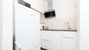 Una cocina compacta con un refrigerador blanco, un microondas y un lavamanos con grifo.