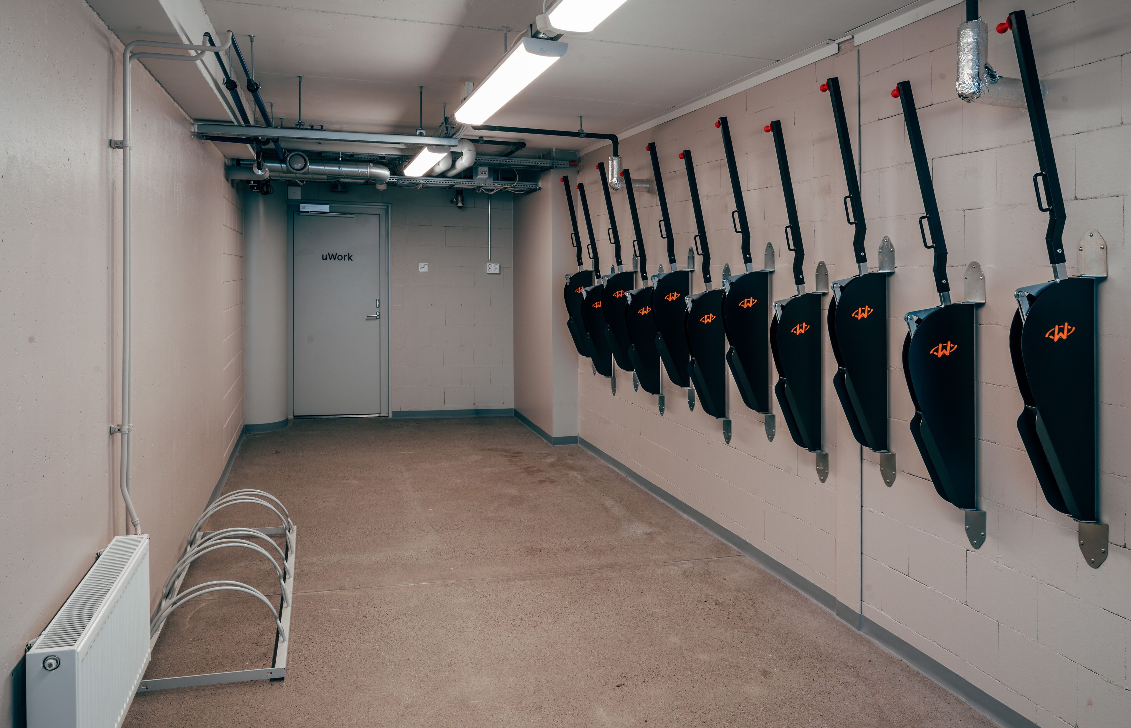 A hallway with a row of black helmets on the wall, a radiator, and a door labeled "uWork".