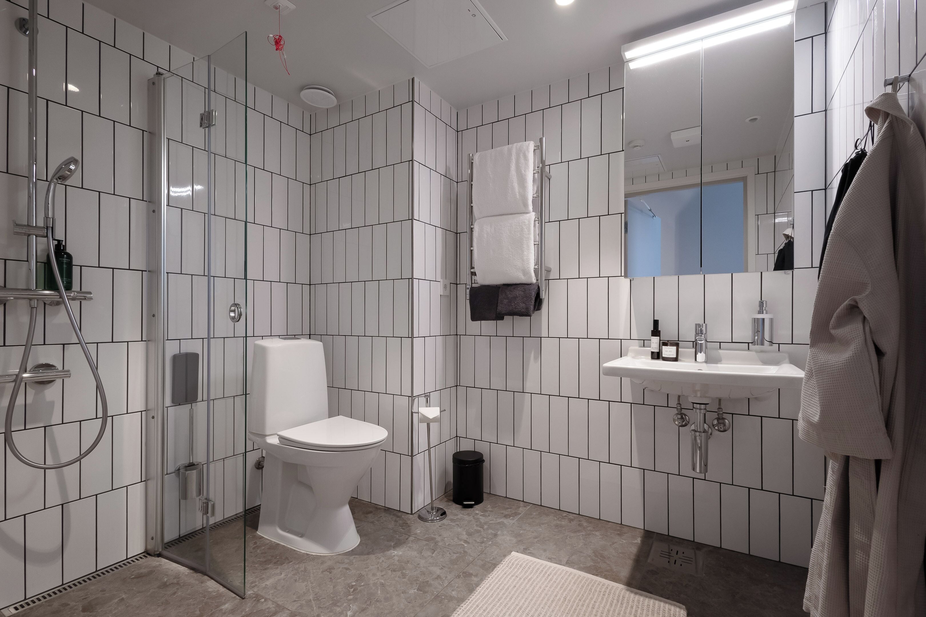 Une salle de bain moderne avec une douche à parois de verre, des toilettes, un lavabo avec un miroir et un porte-serviettes.