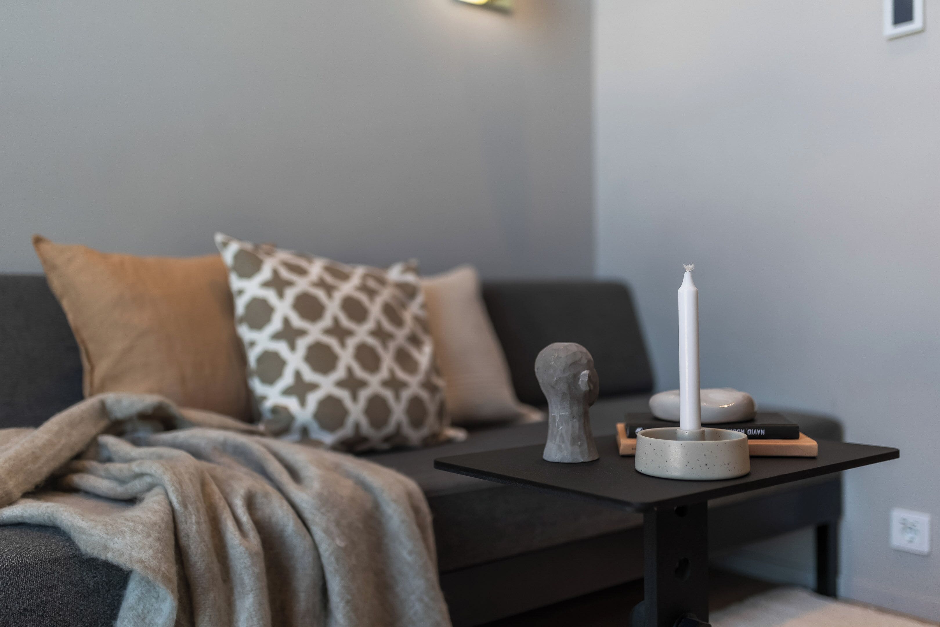 A modern living room with a sofa, patterned pillows, a small table with a candle, and a decorative object.