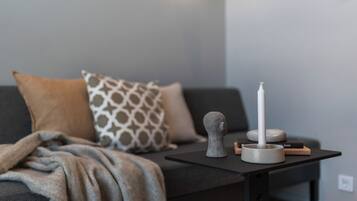 A modern living room with a sofa, patterned pillows, a small table with a candle, and a decorative object.