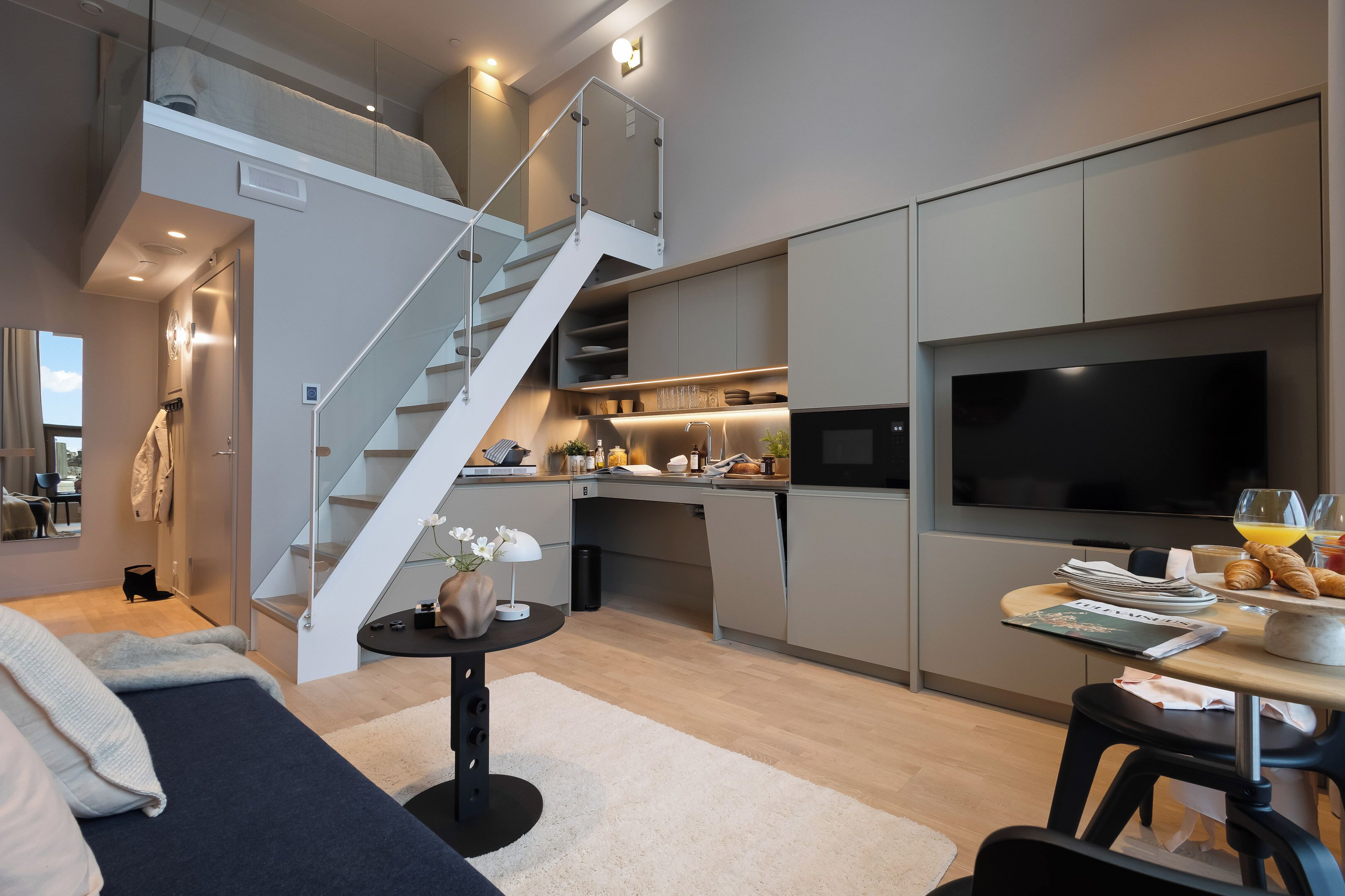 Een moderne keuken met een ingebouwde televisie, een ontbijtgedeelte met etenswaren, en een trap naar een hoger gelegen verdieping.