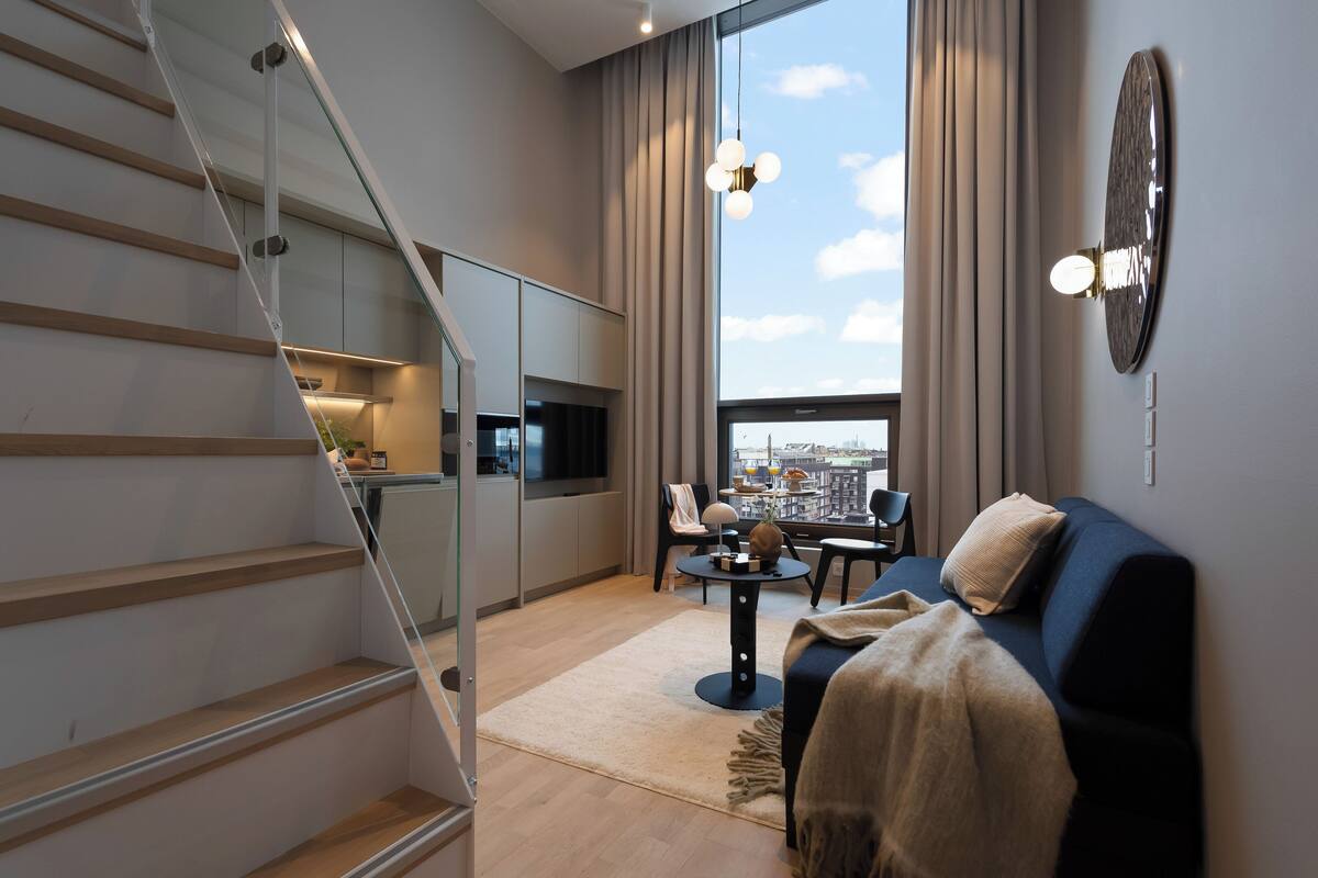 A modern living room with a staircase, a dining area, and a large window offering a city view.